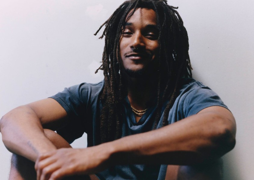 Jordan Ward sat on the ground wearing a blue tshirt and gold chainx